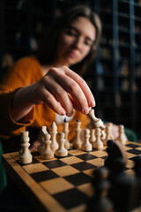 Vertical shot of woman in elegant eyeglasses making chess move sitting on armchair in dark room on...
