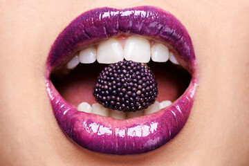 Exotic treats. Shot of a woman wearing purple lipstick and biting into a purple sweet.