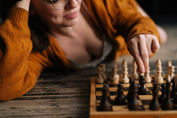Close-up cropped shot of smiling sexy young woman making chess move lying on wooden vintage floor...