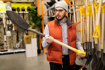 a male customer in a garden tools store chooses a new shovel for earthworks