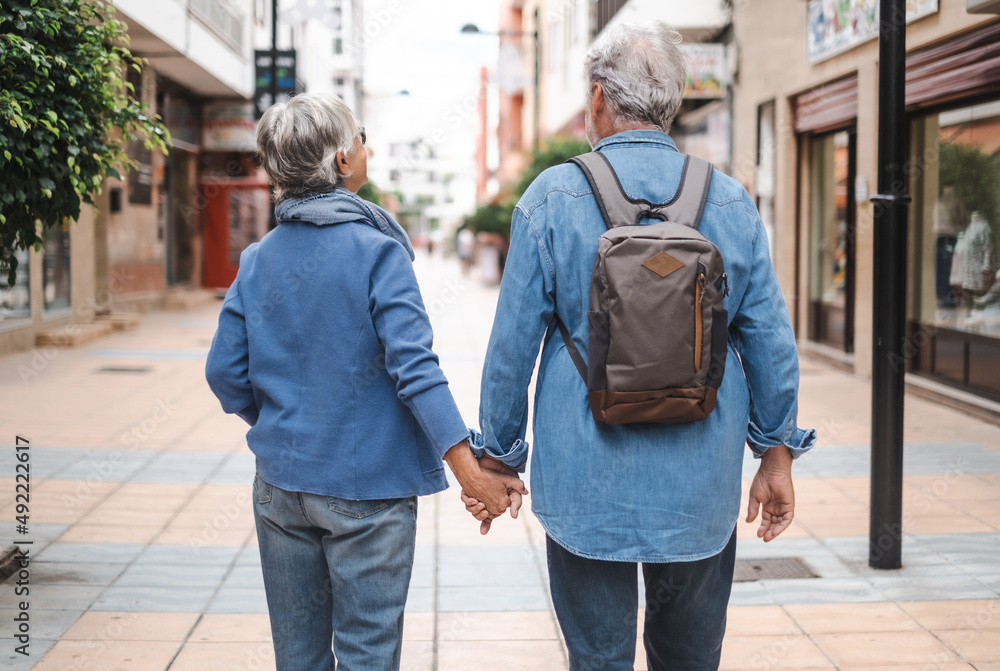 Wall mural back view of senior couple of tourist walking in the city. attractive white haired caucasian people 