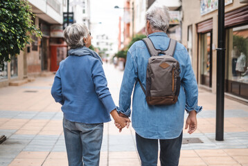 Back view of senior couple of tourist walking in the city. Attractive white haired caucasian people...