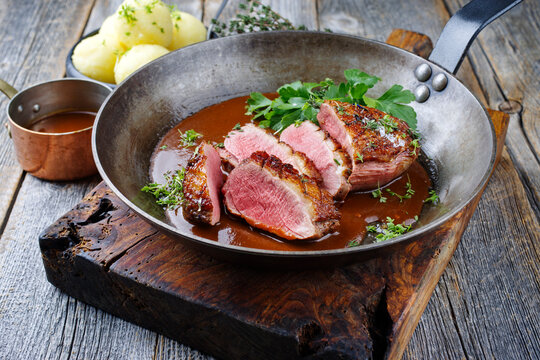 Traditionell gegrilltes Gourmet Entenbrust Filet mit Haut serviert mit Kartoffelknödel in Dunkelbier Sauce als Draufsicht in einer rustikalen Bratpfanne