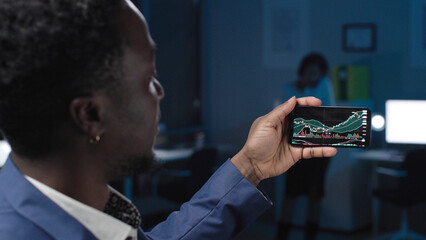 View through shoulder of African-American businessman looking at graphs on smartphone screen