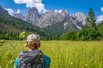 Young woman hiker trekking in a meadow at the base of Pale di San Martin mountain range. San Martino di Castrozza, Trentino, Italy