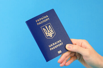 Passport of a citizen of Ukraine in a female hand on a blue background, close-up. Inscription in Ukrainian Ukraine Passport