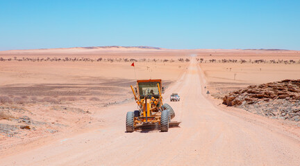 Perspective road background of Yellow grader smooths dirt road in namib deserts - Road grader smoothing a dirt road in a rural area - Namibia, Africa