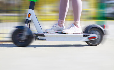 Young woman riding electric kick scooter in the park.