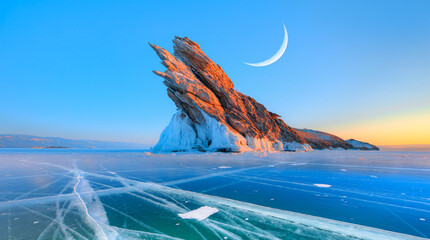 Ogoy island on winter Baikal lake with transparent cracked blue ice at sunrise in the background...