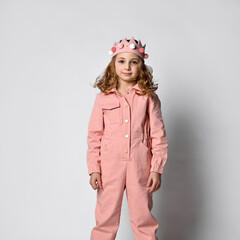 cute girl with a plush crown, standing upright in a dusty rose cotton summer jumpsuit with comfortable pockets. on a light background.