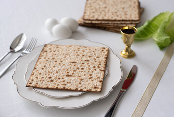 Traditional Holiday table of Jewish with white tablecloth prepared for Passover on plate Matzah with eggs, glass of red wine and leaves green salad.  Fasting time. 