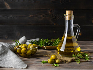 Olive oil of golden color in a transparent jug on a canvas napkin. Olives in a glass vase and sprigs of rosemary in the background. Dark brown wooden background