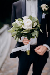 Groom holding a wedding bouquet in the hands standing near bride