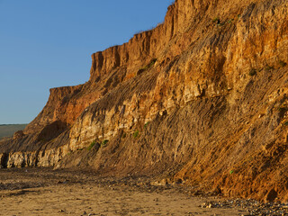 Fototapeta na wymiar A somewhat-abstract view of Compton Bay Cliffs, with the setting autumn sun making the rich warm colours of the rocks glow against the blue sky.