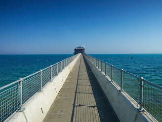 Obraz premium Open, airy seascape looking along the bridge to the lifeboat station at Bembridge with sunlight casting sharp shadows through the railings.