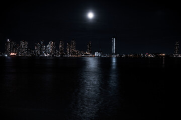 Fototapeta premium A large bright moon shines over the East River from Queens and reveals a city skyline.
