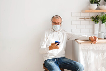 Senior man with medical mask on face using smartphone app for creating playlist music - Elderly male having fun with mobile phone technology copy space - Tech and joyful elderly lifestyle concept