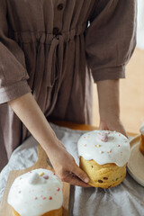 Woman holding baked stylish easter cake with sugar glaze and sprinkles. Homemade easter bread in hands on background of rustic table in room. Happy Easter!