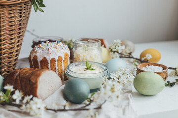 Natural dyed easter eggs, stylish easter bread, ham, beets, butter, cheese on rustic wooden table with spring blossoms. Happy Easter! Traditional Easter basket food for festive dinner