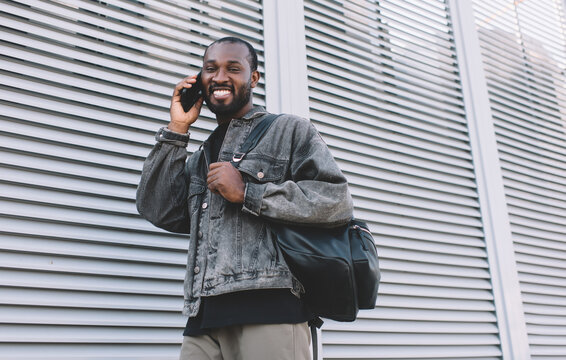 Dark skinned man with travel backpack happy with received international call conversation using roaming in city, portrait of joyful hipster guy using 4g wireless for calling via smartphone app