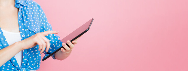 Young woman using a tablet computer on a pink background