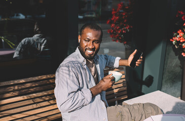 Happy dark skinned man in electronic headphones listening audio book using bluetooth connection at...