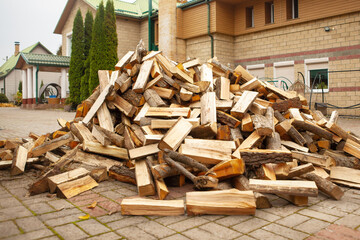 A pile of split firewood for heating the house, unloaded in the yard, against the backdrop of the house, natural heating sources.