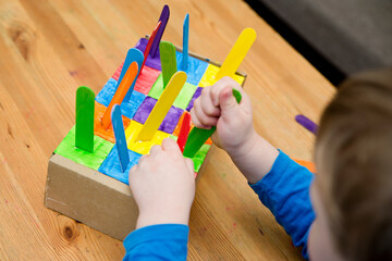 Montessori implement. Sorting by the colors. DIY at home from cardboard box and ice-cream sticks. Easy 5 minute craft. Early preschool education for toddlers. - obrazy, fototapety, plakaty