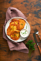 Potato pancakes. Fried homemade potato pancakes or latkes with cream and green onions in rustic plate on old wooden brawn table background. Rustic style. Healthy food. Top view.