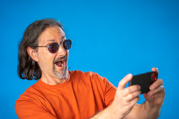 Excited happy fun mature man 50s 60s wears orange shirt showing thumbs up like gesture isolated on solid blue background studio portrait