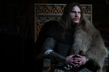 A mighty hero with long hair in chain mail armor in an ancient hall. Medieval warrior in the knight's chambers.