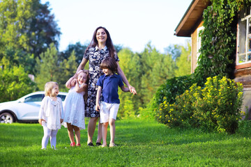 Fototapeta premium Young large family on a summer morning walk. Beautiful mother with children is playing in the park.