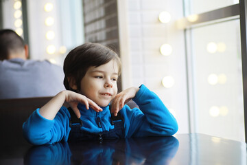 A young boy sits at a table near the window in a cafe and waits for a waiter to come up and take an order.