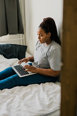 African american young woman using laptop on bed - technologies and communication and social network concept