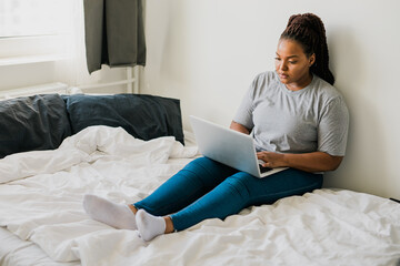 African american young woman using laptop on bed - technologies and communication and social network concept