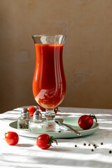 Glass with tomato juice, pepper, salt and tomatoes on the table with white ceiling.