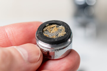 A clogged dirty faucet aerator with calcium plaque in the hand of a plumber. Tap filter above the...