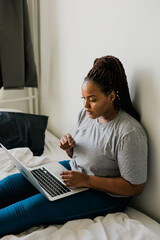 African american young woman using laptop on bed - technologies and communication and social network concept