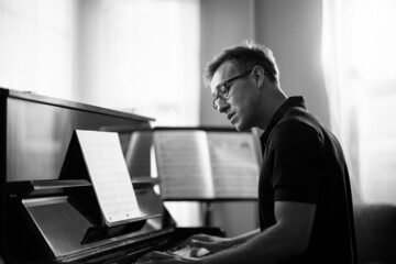 Side view of a man playing piano in music instrument room. Black and white image.