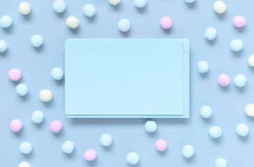 Blank card between pastel pom-poms on light blue top view