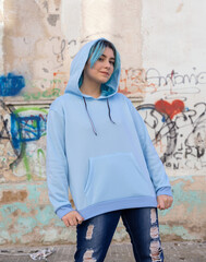 Blue haired Teenage girl in light blue oversize hoodie staying against graffiti wall