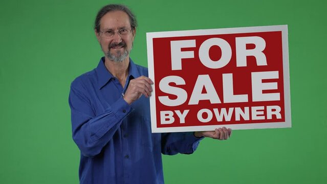 Happy smiling real estate agent holding For Sale By Owner sign on green screen chroma key background with copy space.