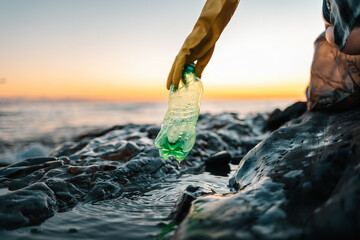 Environmental pollution. Volunteer in protective gloves picks up a plastic bottle on the beach....