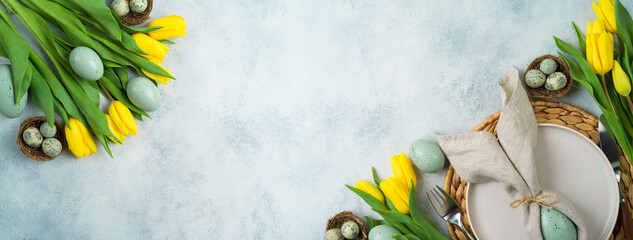 Easter festive table setting with easter eggs decoration and yellow tulips flowers on gray background. Top view with copy space
