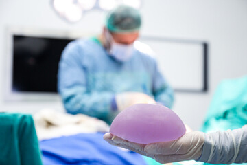 close-up shot at breast implant on nurse's hand during real breast augmentation surgery against...