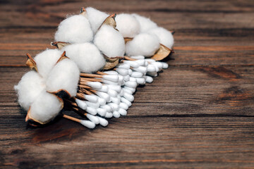 Cosmetic eco sticks on a cardboard base are scattered with cotton on a wooden background.