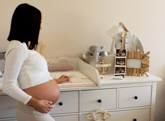 happy pregnant young woman at changing table, in baby nursing room 