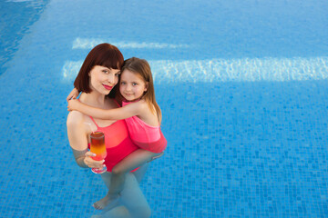 Fototapeta na wymiar Happy family on vacation at an exotic resort. Mom with cocktail teaching her daughter 4 years old to swim in the pool. Top view. Copy space. Happy child and woman playing in swimming pool.