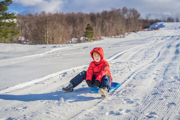 Fototapeta na wymiar happy and positive little boy enjoying sledding and cold weather outdoor, winter fun activity concept