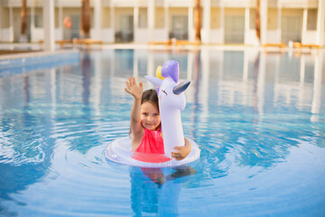 Naklejka premium Child in swimming pool waving her hand . Little girl playing in water. Vacation and traveling with kids. Children play outdoors in summer. Kid with unicorn inflatable ring toy.